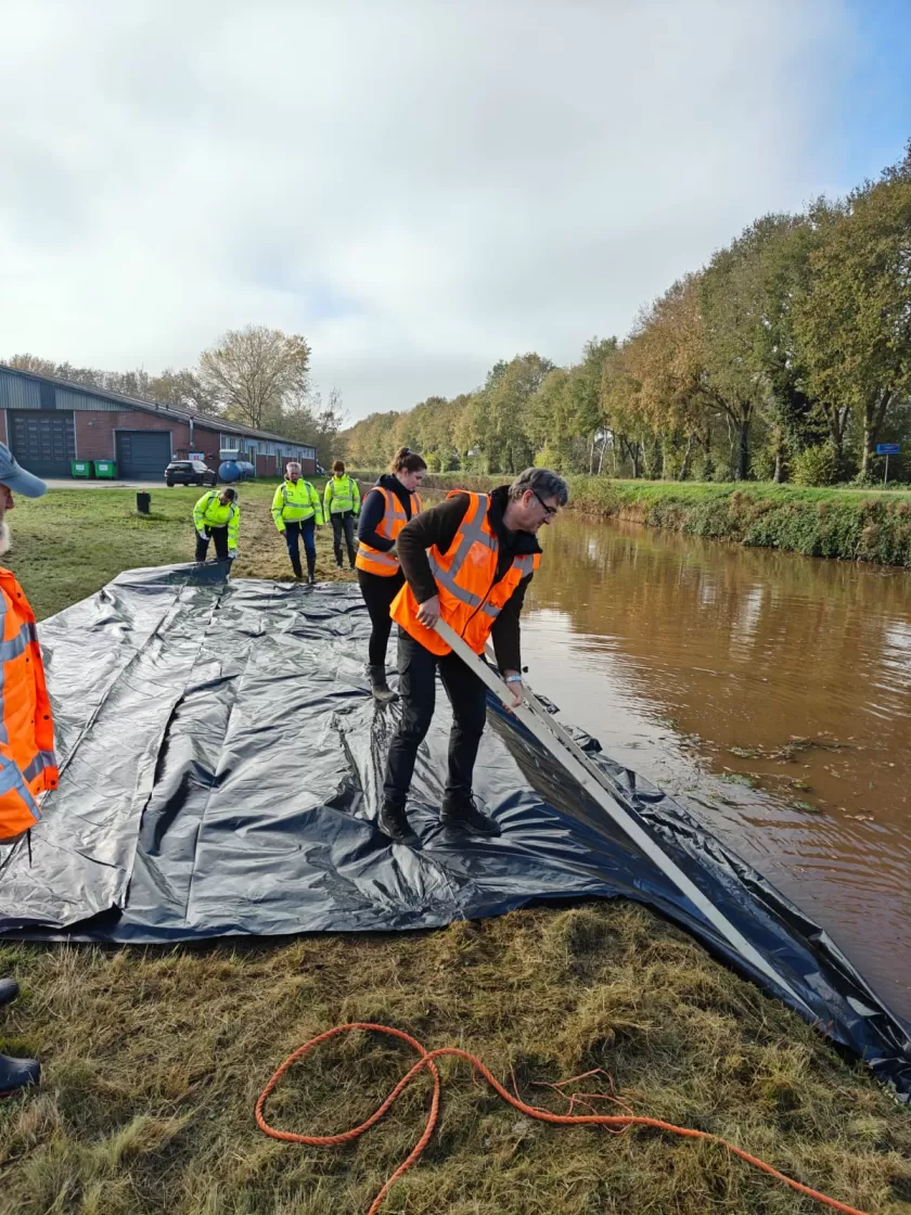 Met stokken ervoor zorgen dat zeil goed tegen buitentalud aan zit