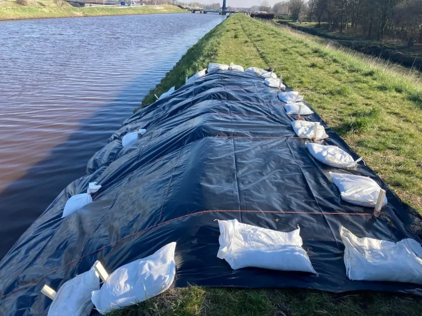Kwelscherm. Zeil op talud met touwen en zandzakken gefixeerd.
